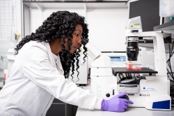 Sigourney Bonner is sitting in a laboratory looking into a microscope