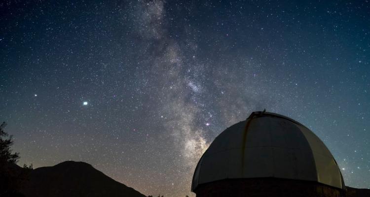 An observatory in the foreground with a night sky showing the Milky Way in the background