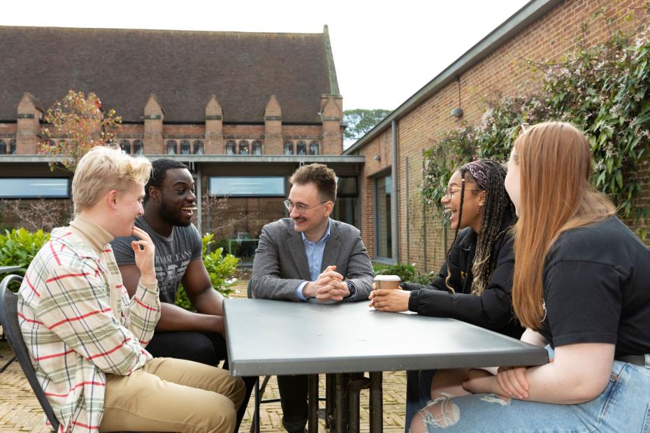 5 students sit talking around a table